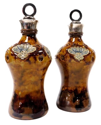 A pair of early 20thC Doulton Lambeth stoneware bottles, with stoppers and silver mount, the stoppers with circular ring tops, of dimpled baluster form moulded with stylised flowers, on a mottled brown ground, impressed marks, London 1901, 26.5cm high.