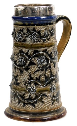 A late 19thC Doulton Lambeth stoneware jug, with silver mount, sgraffito decorated and moulded with three bands of repeating flower heads and leaves, with white jewelling, impressed and incised marks, London 1876, 23.5cm high.