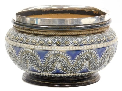 A late 19thC Doulton Lambeth stoneware bowl, with silver mount, sprigged with repeating bands of leaves and stylised flowers, impressed marks, Sheffield 1882, 22cm wide.