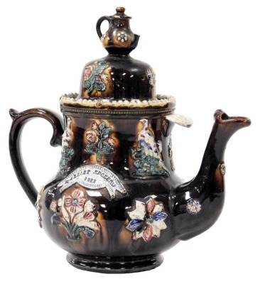 A late 19thC treacle glaze bargeware pottery teapot, with a reserve banner, named for Harriet Edgerton 1882, the lid with a teapot finial, the body moulded, flowers and game birds, 32cm high. (AF)