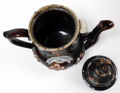 A late 19thC treacle glaze bargeware pottery teapot, with a reserve banner, named for Harriet Edgerton 1882, the lid with a teapot finial, the body moulded, flowers and game birds, 32cm high. (AF) - 3