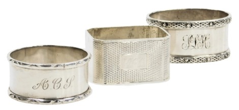 Three silver napkin rings, comprising an oval ring with Celtic band decoration, a circular ring, and an octagonal ring with engine turned decoration, reserve monogram engraved, 2.93oz.