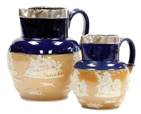 A pair of Doulton Lambeth stoneware graduated two tone harvest jugs, in fawn and cobalt blue, with silver rims, impressed marks, Birmingham 1900, and 1903, 19cm and 40cm high respectively.