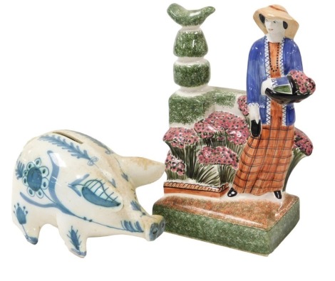 A 20thC Rye pottery figure of The Country Gardener, printed mark, 25cm high together with a Rye pottery piggy bank, painted in blue with flowers and leaves, 17cm wide. (2)