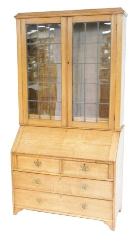 An early 20thC oak bureau bookcase, with an out swept pediment over two leaded glazed doors enclosing two shelves, the bureau with a fall flap opening to reveal a drawer and nine recesses, above two short over two long graduated drawers, raised on bracke