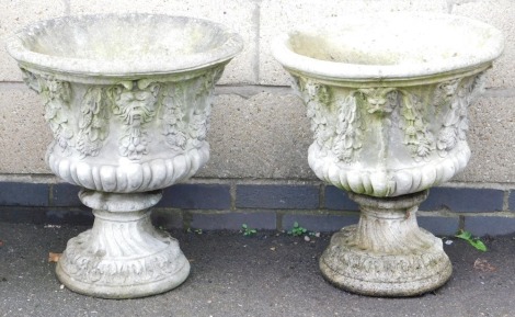 A pair of concrete garden urns, of semi fluted form, moulded with swags and leaves, 58cm high, 53cm wide.