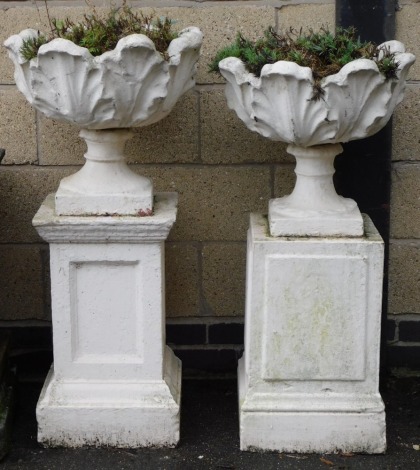 A pair of white painted concrete urns, of circular leaf form, raised on plinths, 107cm high and 102cm high respectively.