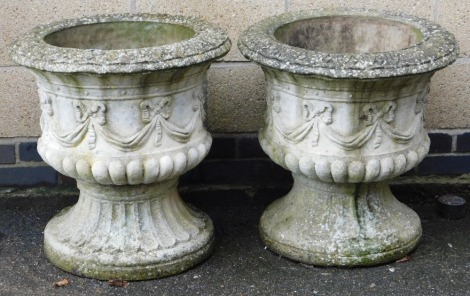 A pair of concrete garden urns, of semi fluted form, decorated with a band of repeating tied bows, 63cm high, 61cm wide.