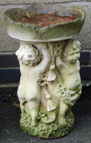 A concrete birdbath, with a flower head shaped bowl, raised on a base of three putti, 52cm high.