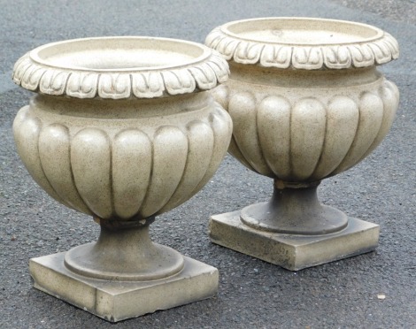 A pair of mottled brown and cream stoneware garden urns, of semi fluted form, with a lappet border, raised on a square base, 42cm high.