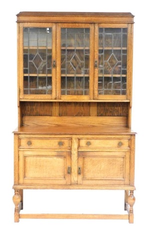 An early 20thC oak dresser, with a domed pediment over three lead glazed doors enclosing two shelves, the base with two drawers over a pair of cupboard doors, raised on turned supports united by a box stretcher, 208cm high, 122cm wide, 48cm deep.