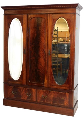 An Edwardian mahogany triple wardrobe, the out swept pediment over a central panel flanked by two doors inset oval bevelled glass, opening to reveal two hanging rails, above two frieze drawers, raised on a plinth base, 204.5cm high, 158cm wide, 54cm deep.