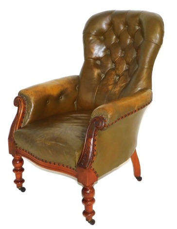 A Victorian mahogany and tan leather balloon back armchair, with button back, foliate carved scroll arms, raised on turned legs, brass capped on castors, 73cm wide.