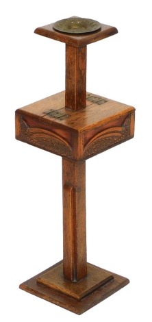 An early 20thC oak smoker's stand, of square section, the top inset with a brass ashtray, above a twin lidded hinged box, with foliate carving, raised on a square column above a stepped square base, 60cm high, 18cm wide, 18cm deep.