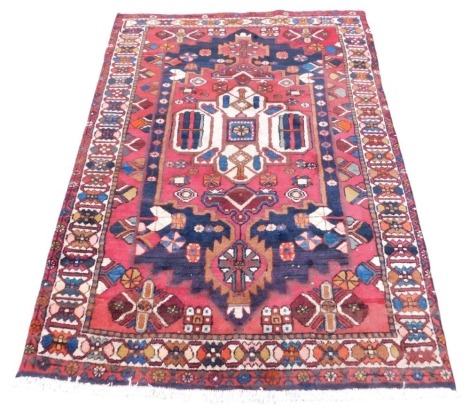 A Persian red ground rug, the central field with a cream medallion, and floral motifs, against an outer field and borders with repeating flowers, 211cm x 152cm.