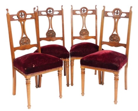 A set of four Victorian Art Nouveau walnut dining chairs, with foliate carved splats, over stuffed seats upholstered in red fabric, raised on turned legs.