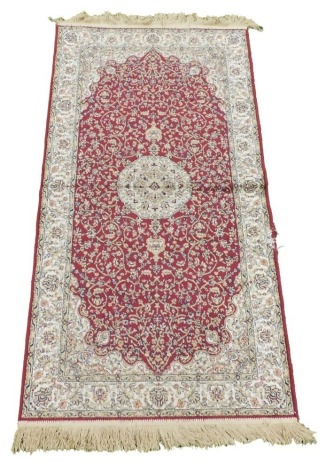 An Isfahan silk red ground rug, decorated with a central medallion, within a field with flowers and foliate scrolls, and repeating floral borders, 146cm x 77cm.