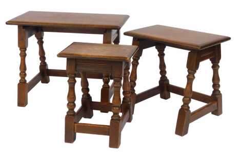 A 20thC nest of three oak tables, on part turned legs united by stretchers, the largest 46cm high, 60cm wide, 34cm deep.