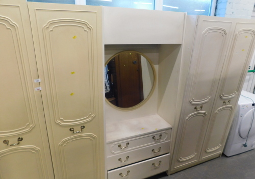 A three sectional bedroom unit, the central section with mirrored back, above three drawers flanked by two double wardrobes, and two bedside chests.