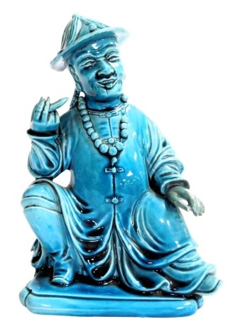 A 19thC Qing dynasty Chinese porcelain figure of a seated gentleman, glazed in turquoise, small object to his right hand, beaded necklace and full flowing gown, 18cm high.