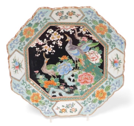 A 19th/20thC Japanese porcelain octagonal plate, the famille noire central panel decorated with peacocks, peonies and apple blossom in coloured enamels, iron red, within wide floral borders signature to base, 33cm diameter.