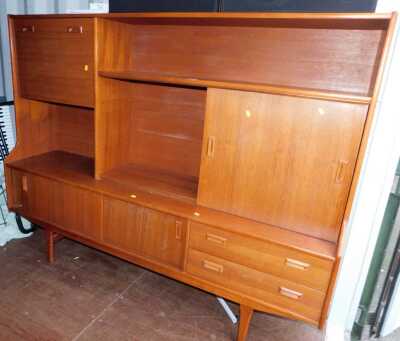 A teak sideboard, the top with an arrangement of sliding doors, recesses and a fall, the base with two sliding doors flanked by two drawers on tapering legs, 143cm high, 183cm wide, 44cm deep.