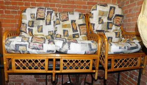 A caned conservatory suite, comprising two seater sofa and an armchair, with loose cushions.