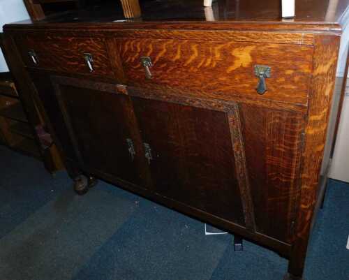 An early 20thC oak sideboard, the raised back inset with a shaped mirror, the base with two drawers above two cupboards, on turned legs, 124cm high, 120cm wide, 48cm deep.