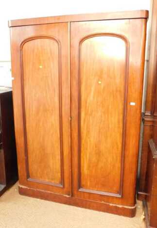 A Victorian mahogany double wardrobe, the top with a rounded edge above two arched panelled doors, enclosing hanging rail flanked by a recess and three drawers, with four further drawers to base, on plinth, 199cm high, 132cm wide, 53cm deep.