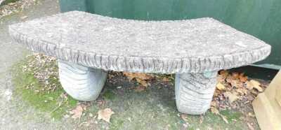 A composition stone garden bench, the top of arched form, on simulated log end supports, 110cm wide.