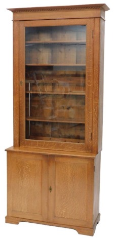 An Edwardian oak bookcase, with dentil cornice, single glazed door over a two door cupboard base, with drawers (probably a former gun cabinet), 223cm high, 96cm wide, 40cm deep.