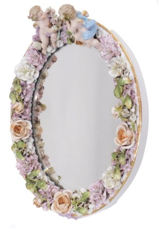 A 19thC Continental oval porcelain wall mirror, mounted with cherubs and encrusted with floral decoration, 39cm high.