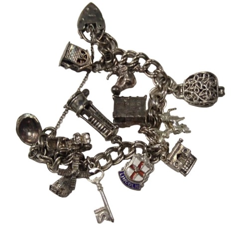 A charm bracelet, on double curb link bracelet with safety chain and heart shaped padlock, various charms including miner's lamp, typewriter, elephant on ball, etc., the chain 16cm long, white metal stamped 925, 43.7g all in.