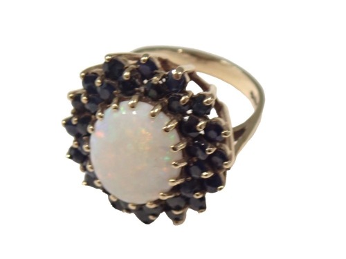 A 9ct gold opal and sapphire dress ring, of chunk design, the central opal 5.4mm x 2.4mm, surrounded by layers of sapphires, in raised claw basket setting, each stone claw set, ring size Q½, 7.8g all in.