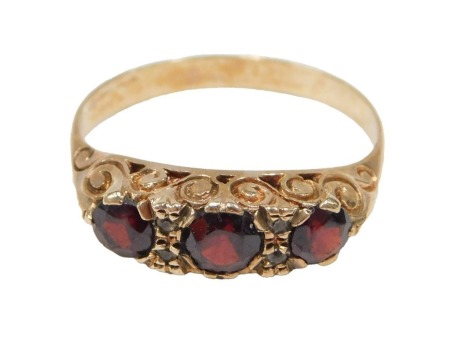 A three stone garnet dress ring, set with three round brilliant cut garnets and two tiny diamonds, on scroll design shoulders, yellow metal unmarked, ring size V½, 3.7g all in.