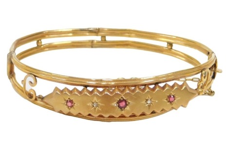 A Victorian half hinged bangle, the central design set with five stones comprising three rubies and two diamonds, on open work setting, yellow metal unmarked, with safety chain, 6cm diameter, 7.9g all in.