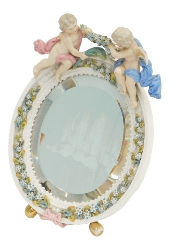 A Dresden porcelain table mirror, decorated with cherubs (AF), with a wooden easel back and Augustus Rex monogram, 30cm high.