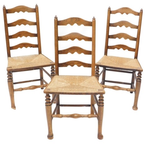 An associated set of three 19thC Lancashire style oak and ash ladder back chairs, each with a rush seat.