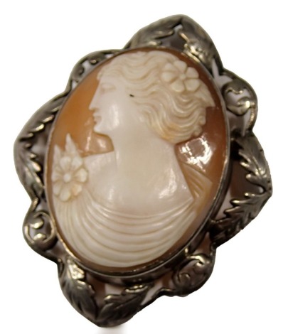 A shell cameo brooch, the oval cameo depicting maiden in flowing robes with flowers, in a rub over leaf moulded and pierced border, on single pin back, white metal unmarked, 6cm x 4cm, 16.7g all in. (AF)