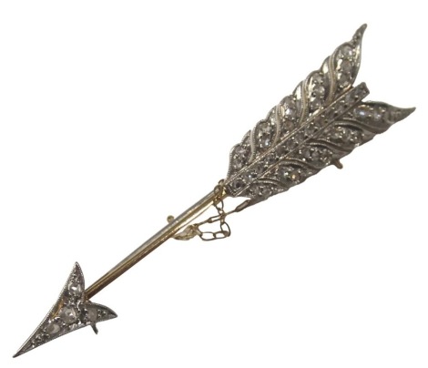 An arrow brooch, on a yellow and white gold setting, set with tiny diamonds, on a feathered bow, yellow metal unmarked, with part safety chain, 5cm long, 4.4g all in. (AF)