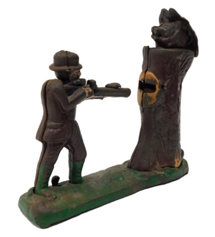 A cast iron painted money box, modelled in the form of a hunter beside a bear within a tree stump, 23cm wide.