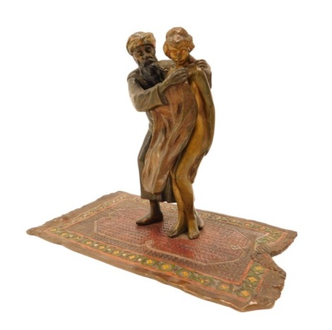 An erotic cold painted bronze figure group in the manner of Bergmann, modelled in the form of an Arab gentleman with articulated arm beside a nude female, standing on a Persian carpet, 13cm high.