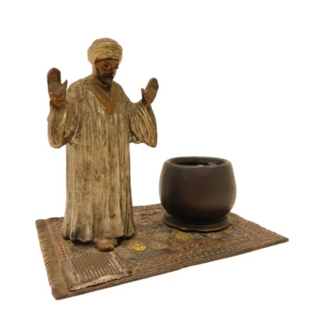 A cold painted metal match stand, modelled in the form of a gentleman with arms raised beside a pot or cauldron, standing an Oriental carpet with ridges for matches, 16cm wide.