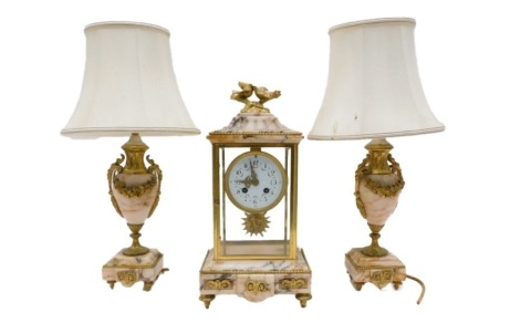 A late 19th/early 20th French gilt metal and marble clock garniture, the clock with enamel dial and Arabic numerals, embellished with floral swags, in four glass case, on toupee, 40cm high, flanked by a pair of two handled urns, (AF), converted to electri