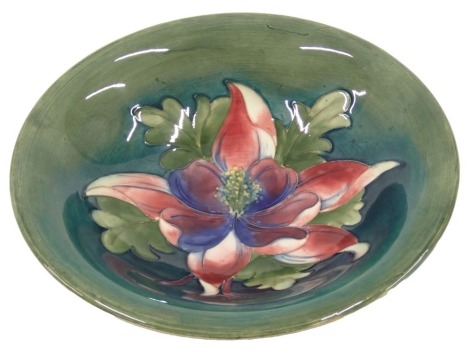 A Moorcroft shallow pottery bowl, decorated centrally with blue and pink flowers, surrounded by leaves, on a blue and green shaded ground, impressed and hand scripted marks to underside, 25cm diameter.