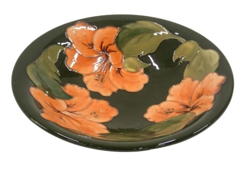 A Moorcroft pottery ceramic bowl, decorated with coral coloured flowers and leaves on a green ground, handwritten marks to underside, 25cm diameter.