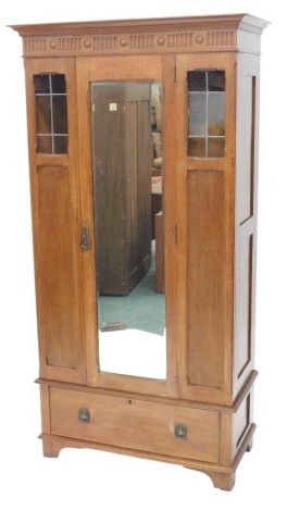 A early 20thC oak wardrobe, the moulded cornice carved with flutes and roundels, above a mirrored door, flanked by panels and leaded glazed sections, the base with a drawer on bracket feet, 198cm high, 91cm wide.