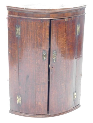 An early 19thC oak and mahogany cross banded bow fronted corner cabinet, 95cm high, 66cm wide.