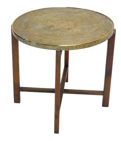 An Eastern brass occasional tray top table, decorated with script, geometric devices, etc., on a folding stand, 49cm diameter.