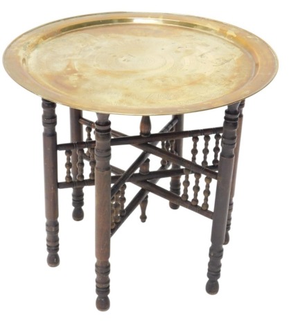 An Eastern brass Benares style tray table, the circular top engraved with geometric and similar devices, on a folding stand, with turned supports, 59cm diameter.